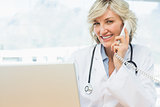 Smiling female doctor using laptop and phone
