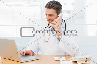 Concentrated doctor using laptop and phone