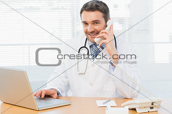 Male doctor using laptop and phone in medical office
