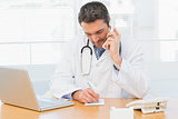Doctor using phone while writing notes at medical office
