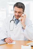Concentrated doctor using phone while writing notes