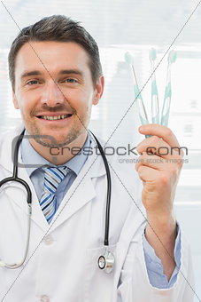 Smiling doctor holding toothbrushes in office