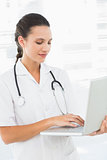 Concentrated young female doctor using laptop