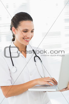 Concentrated smiling female doctor using laptop