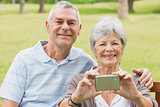 Cheerful senior couple photographing themselves at park