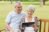 Senior couple using digital tablet on bench at park