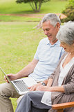 Smiling senior couple using laptop at park