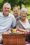 Smiling senior couple and granddaughter with picnic basket at park