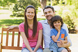 Smiling couple with son sitting on park bench