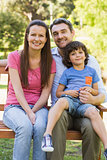 Smiling couple with son sitting on park bench