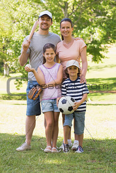 Family of four holding baseball bat and ball in park