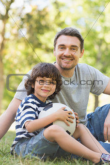 Father and son with football sitting on grass inpark