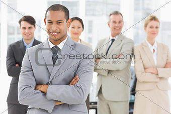 Young businessman smiling at camera with team behind him