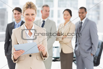 Happy businesswoman using her tablet with team behind her