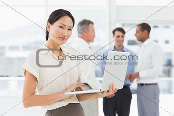 Asian businesswoman using laptop with team behind her