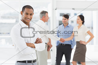 Young businessman with team behind him smiling at camera