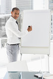 Young smiling businessman presenting at whiteboard with marker