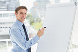 Young smiling businessman writing on whiteboard with marker