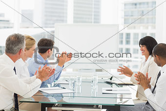 Business people clapping at blank whiteboard in conference room
