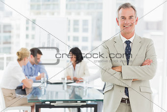 Happy businessman looking at camera while staff discuss behind him