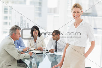 Happy businesswoman looking at camera while staff discuss behind her