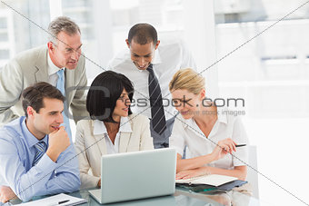 Happy business people gathered around laptop talking