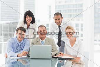 Happy business people gathered around laptop looking at camera