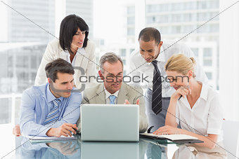 Happy business people gathered around laptop looking at it