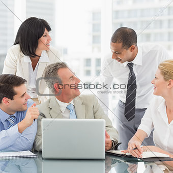 Happy business team gathered around laptop chatting