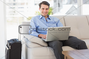 Travelling businessman using laptop sitting on the couch smiling at camera