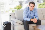 Smiling businessman sitting on couch waiting to leave on business trip