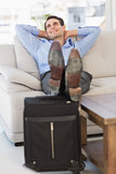 Smiling businessman relaxing on couch with feet up on suitcase