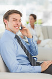 Smiling businessman on the phone sitting on sofa