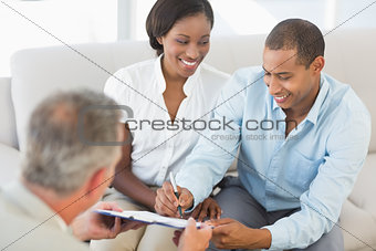 Young smiling couple signing contract on the couch