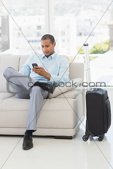 Businessman sending a text sitting on sofa waiting to depart on business trip