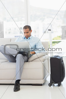 Businessman using laptop sitting on sofa waiting to depart on business trip