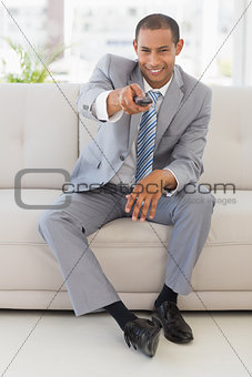Smiling businessman sitting on couch using remote