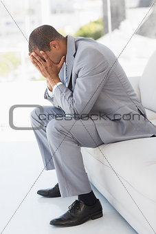 Worried businessman sitting on couch with head in hands