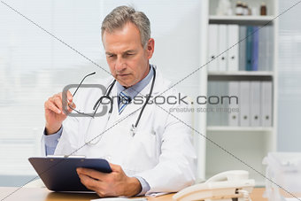 Concentrating doctor sitting at his desk with clipboard