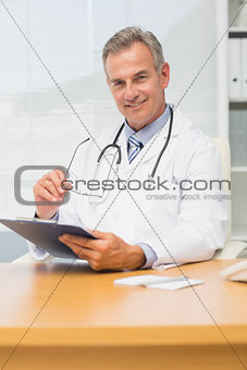 Smiling doctor sitting at his desk with clipboard