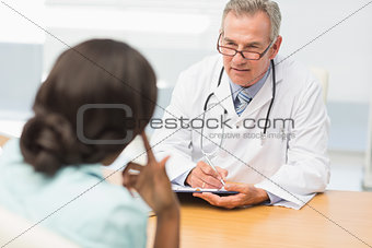 Mature doctor listening to his patient and taking notes