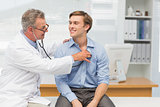 Mature doctor listening to his happy patients chest with stethoscope