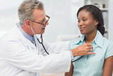 Doctor listening to cheerful young patients chest with stethoscope