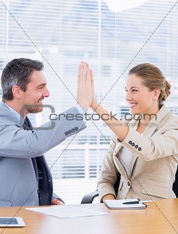 Smartly dressed colleagues giving high five in business meeting