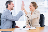 Smartly dressed colleagues giving high five in business meeting