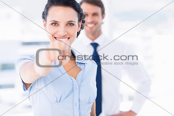 Happy woman pointing at camera with colleague in background