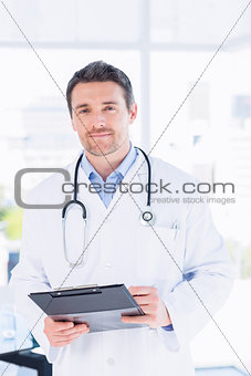 Confident male doctor with clipboard in hospital