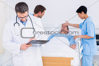 Doctor writing reports with patient and surgeon in background