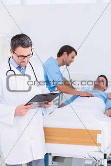 Doctor writing reports with patient and surgeon in background