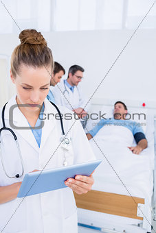Doctor using digital tablet with colleagues and patient behind